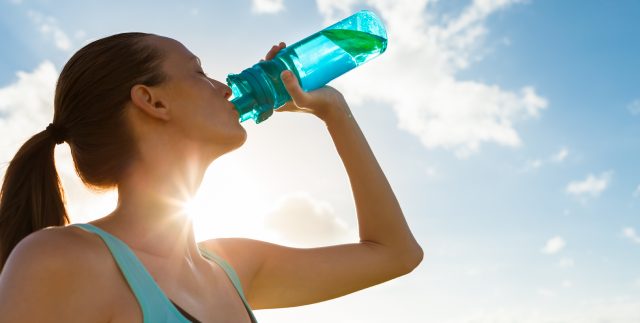 A dehydrated woman chugs a water bottle in the Houston, TX sun