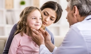 An emergency room doctor checks a girl's neck glands with her mother at a Houston, TX emergency room