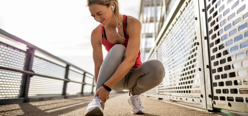 Sprain - A female winces while touching her ankle on a run in Houston, TX